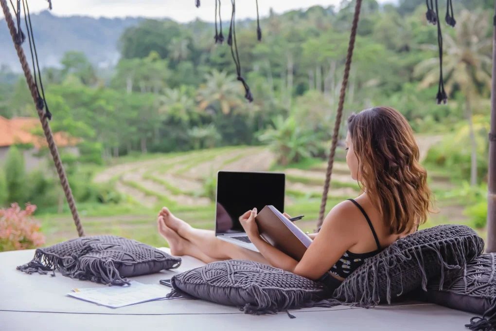 A digital nomad working on a laptop in a bamboo cafe in Bali.